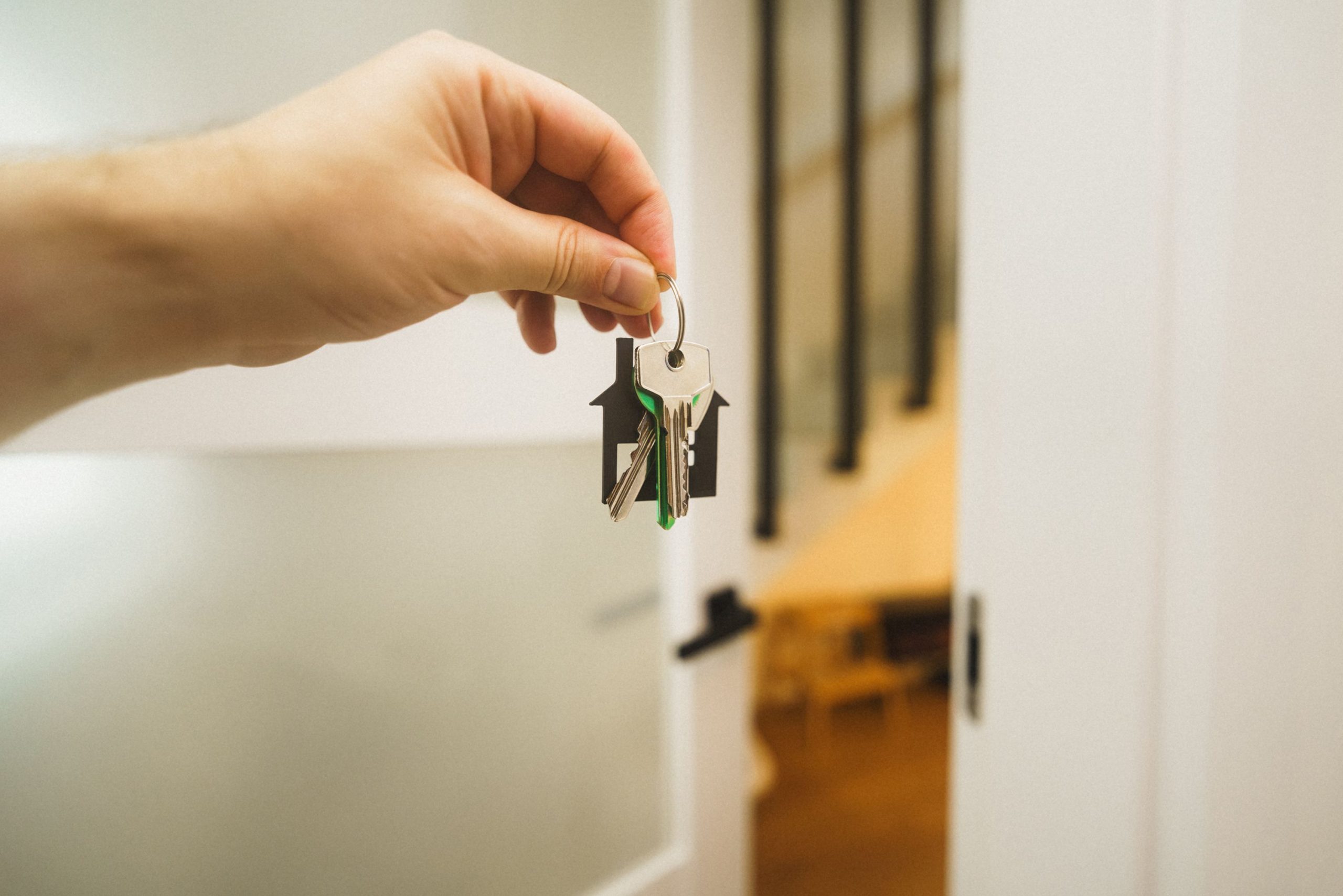 A hand holding a house key indoors signifies new ownership or leasing in real estate.